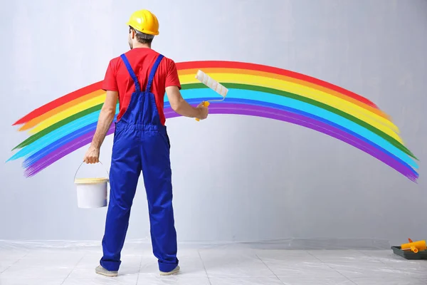 Young worker and painted rainbow on wall in room — Stock Photo, Image