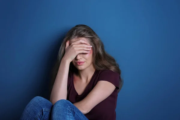 Gehavende triest vrouw zitten alleen in de buurt van blauwe muur — Stockfoto