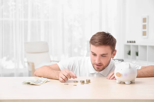 Jovem com banco porquinho à mesa — Fotografia de Stock