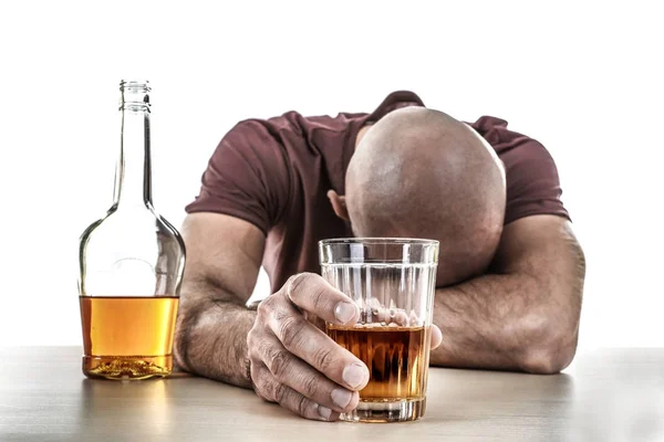 Hombre borracho con vaso y botella de bebida alcohólica sentado en la mesa sobre fondo blanco — Foto de Stock