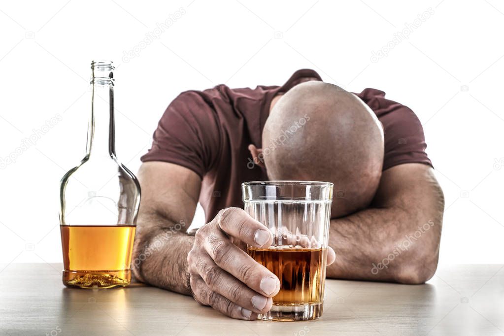 Drunk man with glass and bottle of alcohol drink sitting at table on white background