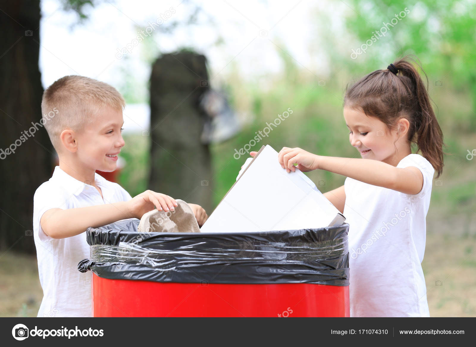 Kleine Kinder werfen Müll in Mülleimer im Freien - Stockfotografie