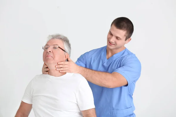 Fisioterapeuta trabalhando com paciente sênior em fundo claro — Fotografia de Stock