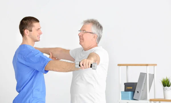 Fisioterapeuta trabajando con un paciente mayor en una clínica moderna —  Fotos de Stock