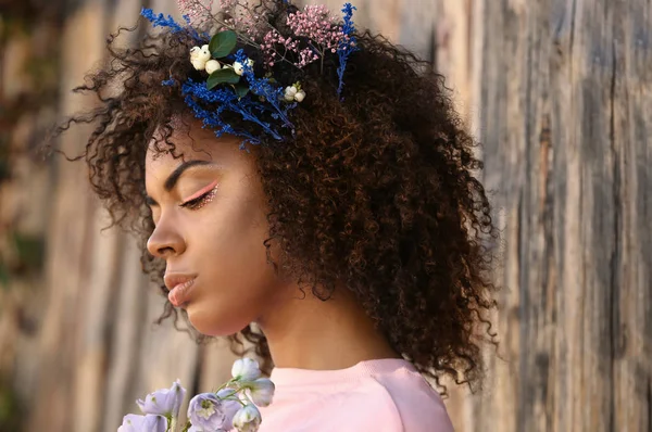 Gyönyörű fiatal afro-amerikai nő, virágokkal, haj, fából készült háttér — Stock Fotó