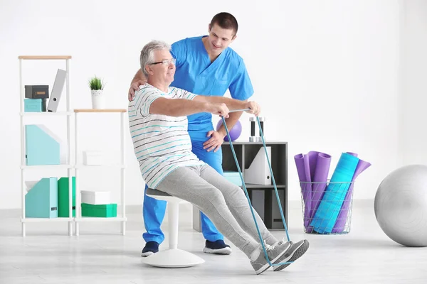Fisioterapeuta trabajando con un paciente mayor en una clínica moderna — Foto de Stock