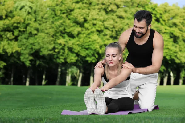 Sportieve jongedame met trainer doen oefening in groen park — Stockfoto