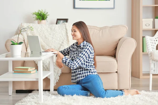 Mooie vrouw met moderne laptop zitting op tapijt thuis — Stockfoto