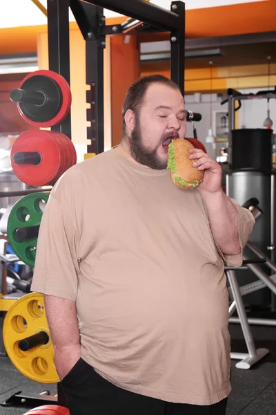 Hombre con sobrepeso comiendo sándwich en gimnasio —  Fotos de Stock