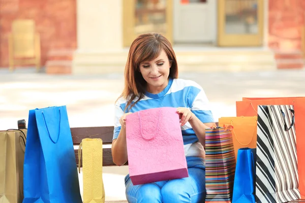Attraktive reife Frau mit Einkaufstaschen sitzt auf Bank im Freien — Stockfoto