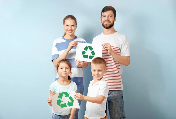 Family holding paper sheets with recycling symbol on color background — Stock Photo, Image