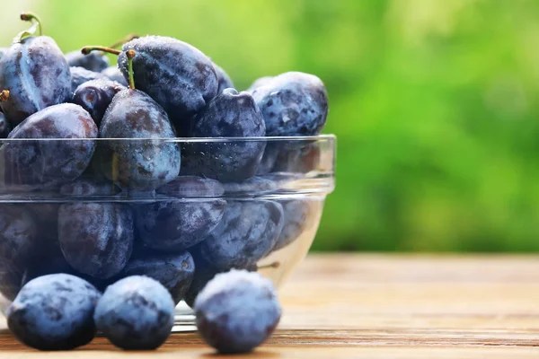 Ciotola di vetro con gustose prugne mature sul tavolo all'aperto — Foto Stock