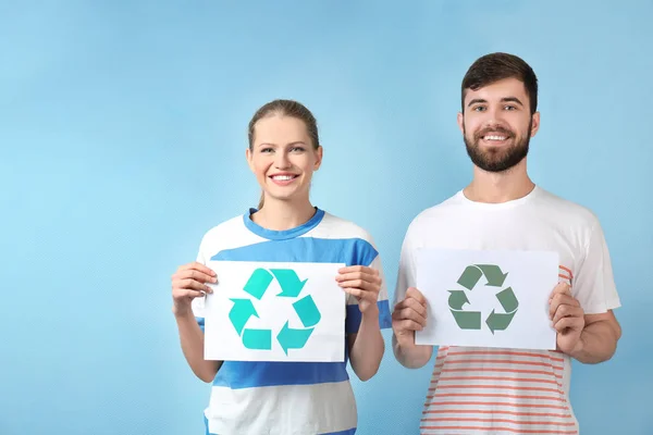 Pareja joven sosteniendo hoja de papel con símbolo de reciclaje en el fondo de color — Foto de Stock