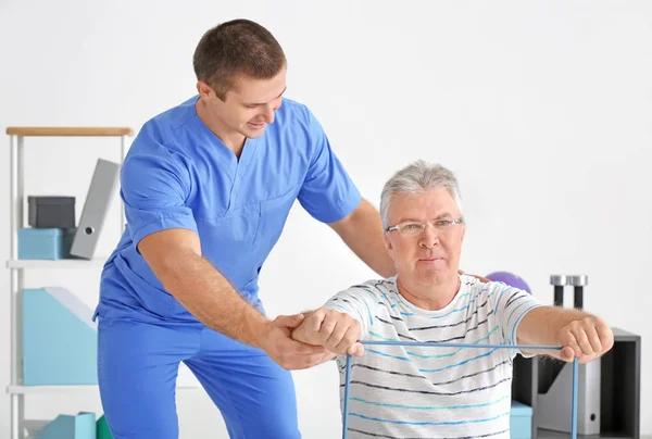 Fisioterapeuta trabalhando com paciente sênior na clínica moderna — Fotografia de Stock