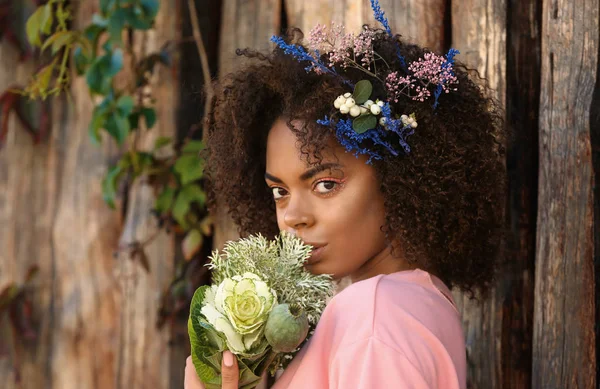 Vackra unga afroamerikanska kvinna med blommor mot trä bakgrund — Stockfoto
