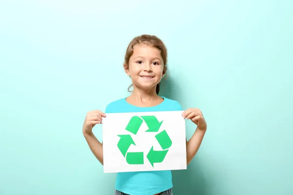 Little girl holding paper sheet with recycling symbol on color background — Stock Photo, Image