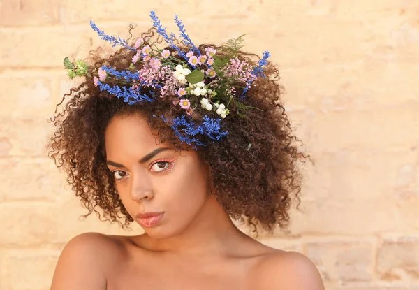Vackra unga afroamerikanska kvinna med blommor i håret mot tegelvägg — Stockfoto