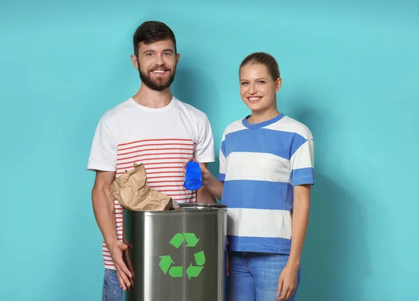 Casal jovem com lixeira no fundo da cor. Conceito de reciclagem — Fotografia de Stock