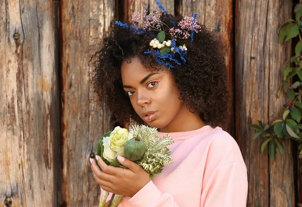 Bella giovane donna afro-americana con fiori sullo sfondo in legno — Foto Stock