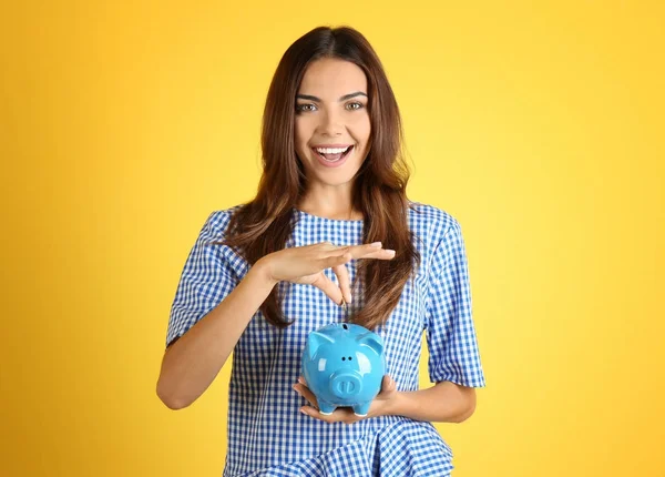 Bella giovane donna con salvadanaio su sfondo a colori — Foto Stock