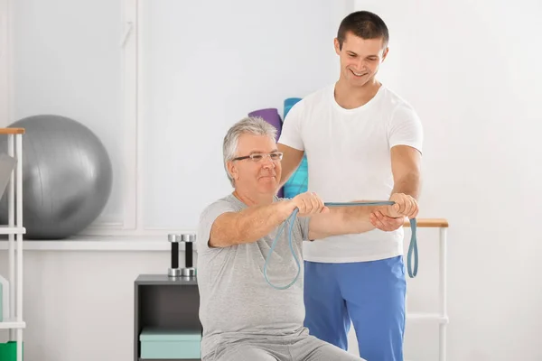 Fisioterapeuta trabajando con un paciente mayor en una clínica moderna —  Fotos de Stock