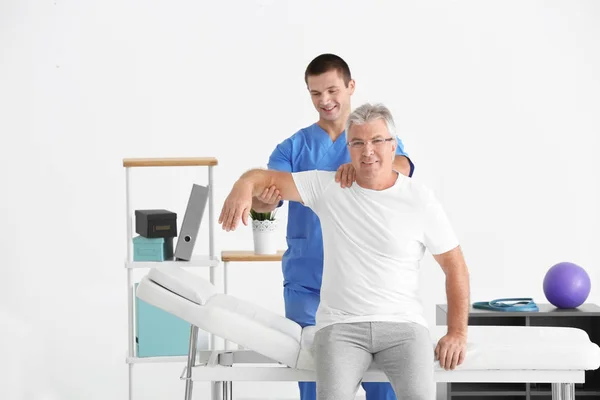 Fisioterapeuta trabalhando com paciente sênior na clínica moderna — Fotografia de Stock