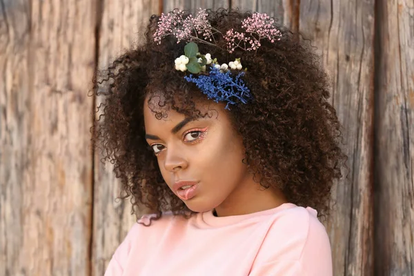 Vackra unga afroamerikanska kvinna med blommor i håret mot trä bakgrund — Stockfoto