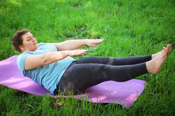 Överviktig kvinna träning på gräs — Stockfoto