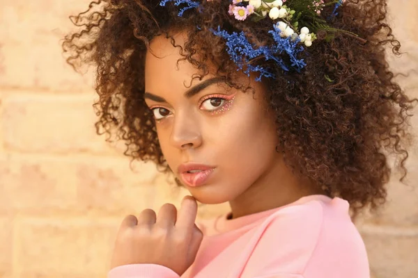 Vackra unga afroamerikanska kvinna med blommor i håret mot tegelvägg — Stockfoto