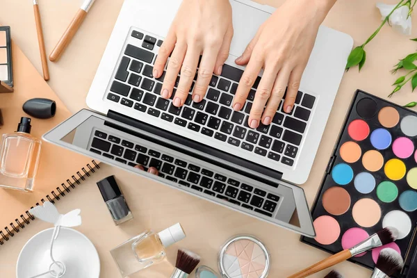 Mains de blogueur beauté avec ordinateur portable moderne et différents articles pour femmes sur la table — Photo