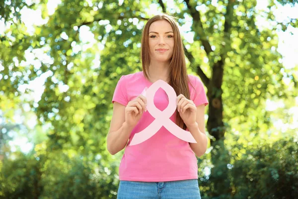 Mujer joven en camiseta rosa que sostiene la cinta de conciencia del cáncer de mama al aire libre — Foto de Stock