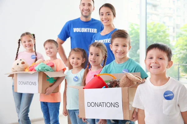 Voluntarios felices con niños sosteniendo cajas de donación en el interior —  Fotos de Stock
