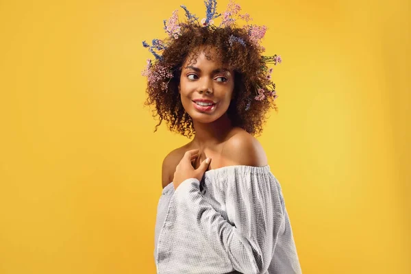 Bela jovem afro-americana com flores no cabelo contra fundo de cor — Fotografia de Stock