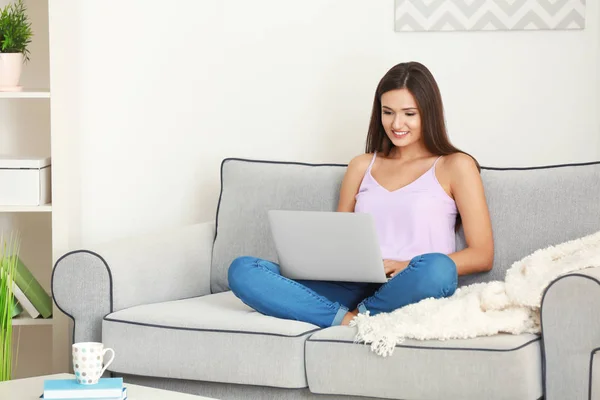 Mulher bonita com laptop moderno sentado no sofá em casa — Fotografia de Stock