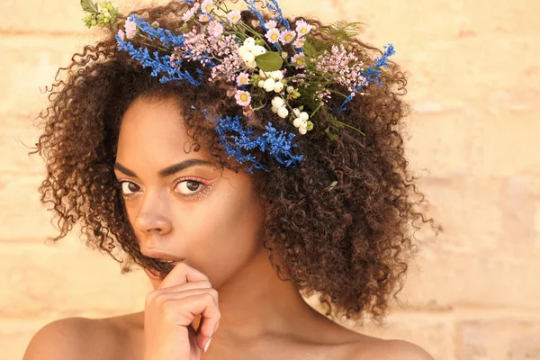 Bela jovem afro-americana com flores no cabelo contra a parede de tijolo — Fotografia de Stock