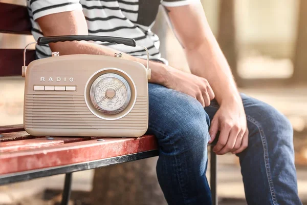 Young man with retro radio sitting on bench outdoors