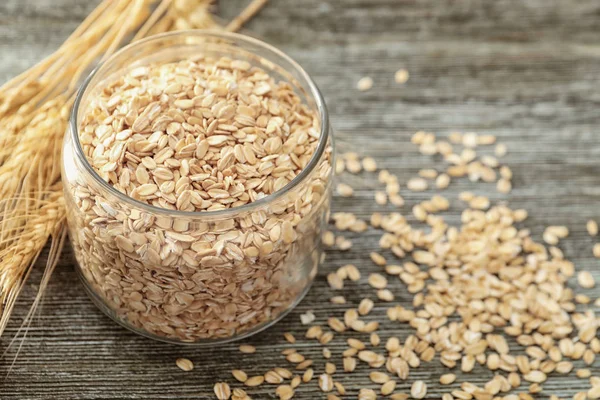 Tarro de vidrio con copos de avena sobre fondo de madera —  Fotos de Stock