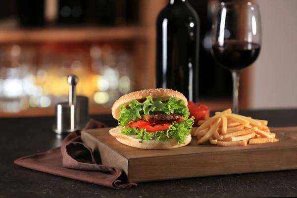 Tabla de madera con deliciosas papas fritas y hamburguesa en la mesa en el restaurante — Foto de Stock
