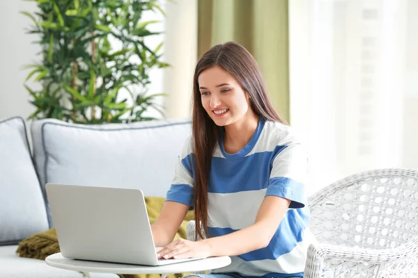 Hübsche Frau mit modernem Laptop sitzt im Sessel zu Hause — Stockfoto