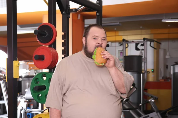 Homem com excesso de peso comendo sanduíche no ginásio — Fotografia de Stock