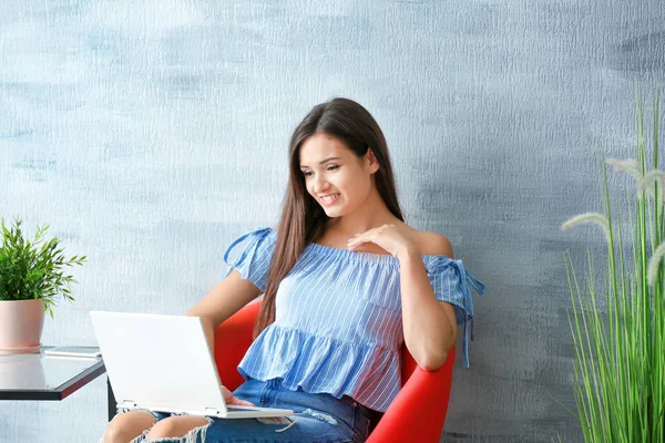 Красивая женщина с современным ноутбуком сидит в кресле дома — стоковое фото