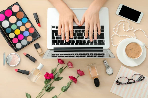 Mains de blogueur beauté avec ordinateur portable moderne et différents articles pour femmes sur la table — Photo