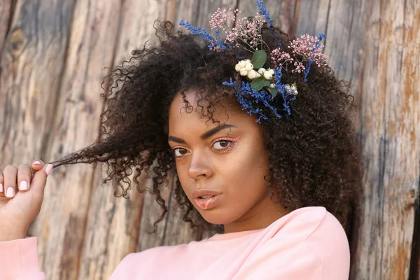 Krásná mladá americká žena s květinami ve vlasech dřevěné pozadí — Stock fotografie