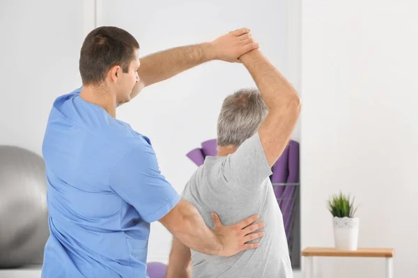 Fisioterapeuta trabajando con un paciente mayor en una clínica moderna —  Fotos de Stock