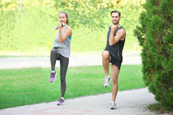 Young man and woman doing exercises in park — Stock Photo, Image