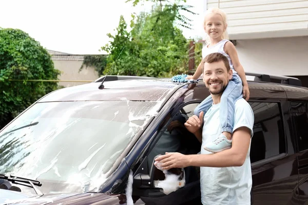 Man with little daughter washing car outdoors