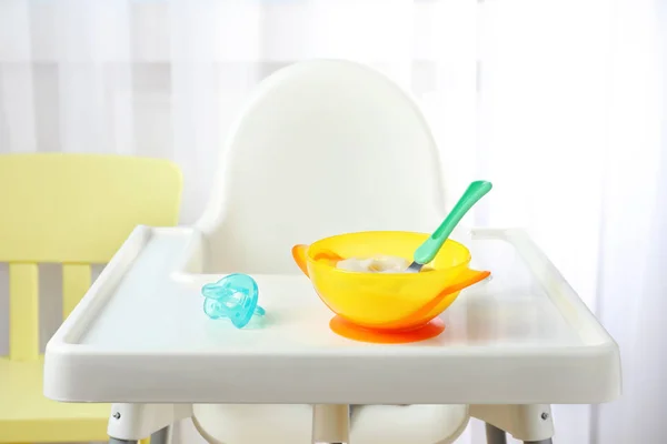 Skål med barnmat på barnstol inomhus — Stockfoto