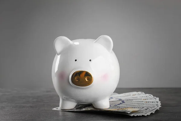 Niedliches Sparschwein mit Geld auf dem Tisch vor grauem Hintergrund — Stockfoto