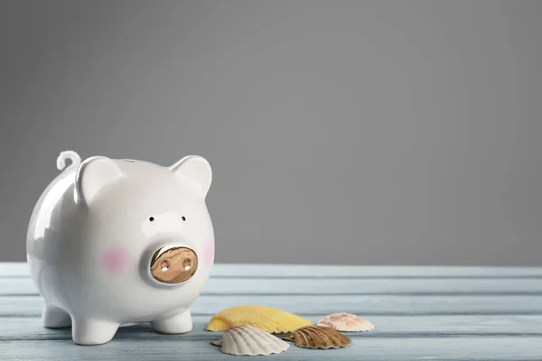 Niedliches Sparschwein mit Muscheln auf Holztisch vor grauem Hintergrund — Stockfoto