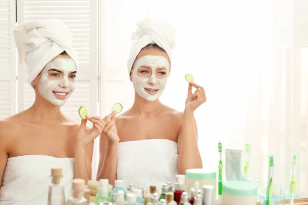 Jeunes femmes avec masques faciaux et tranches de concombre dans la salle de bain — Photo